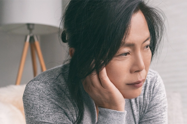 Adrenal-Fatigue-Doctor A middle-aged asian woman sitting on her couch, resting her head on her hand, suffering from adrenal fatigue. Get treatment for adrenal fatigue syndrome from Anita Petruzzelli, M.D. in Glastonbury.