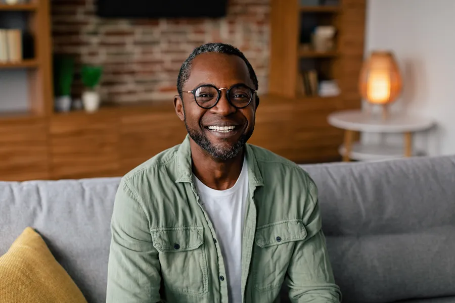 Andropause-Doctor A middle aged black man in a green button up shirt sits on his couch smiling, happy with his treatment for andropause and low testosterone from Anita Petruzzelli, M.D. in Glastonbury.