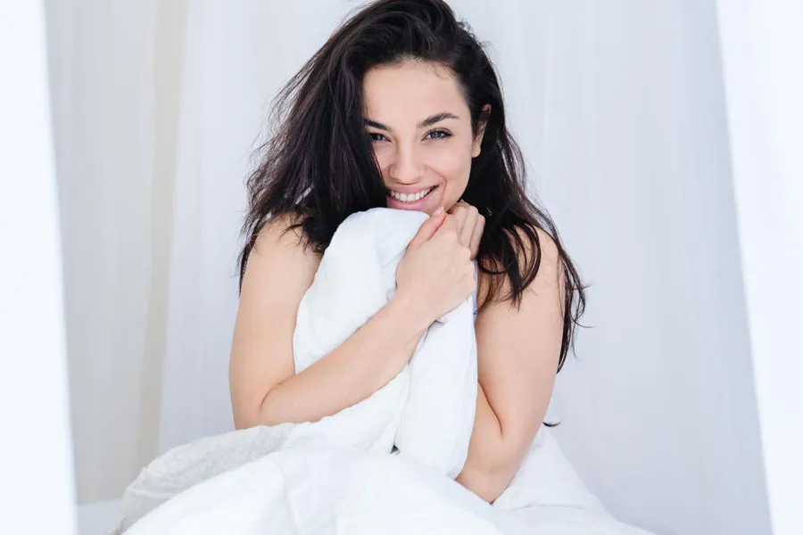 Female-Sexual-Dysfunction-Clinic A woman smiling and holding the sheets up to her chin in bed. Get medications for female sexual dysfunction from Anita Petruzzelli, M.D. in Glastonbury.