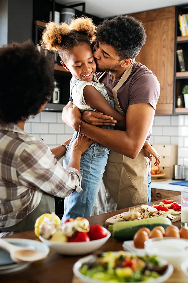 Gut-Health-Treatment A man holds his daughter and kisses her cheek as the family makes a healthy dinner in the kitchen. Get help for digestive issues and gut health from Anita Petruzzelli, M.D. in Glastonbury.