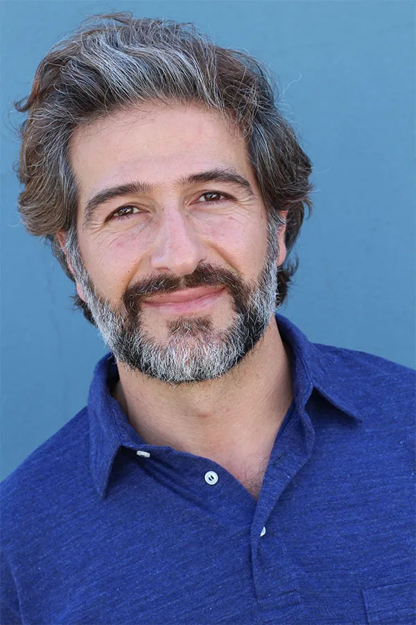 Hair-Loss-Treatment Image of a cheerful man with a bright smile and curly hair against a natural landscape. Anita Petruzzelli, M.D. provides personalized hair loss treatments in Glastonbury.