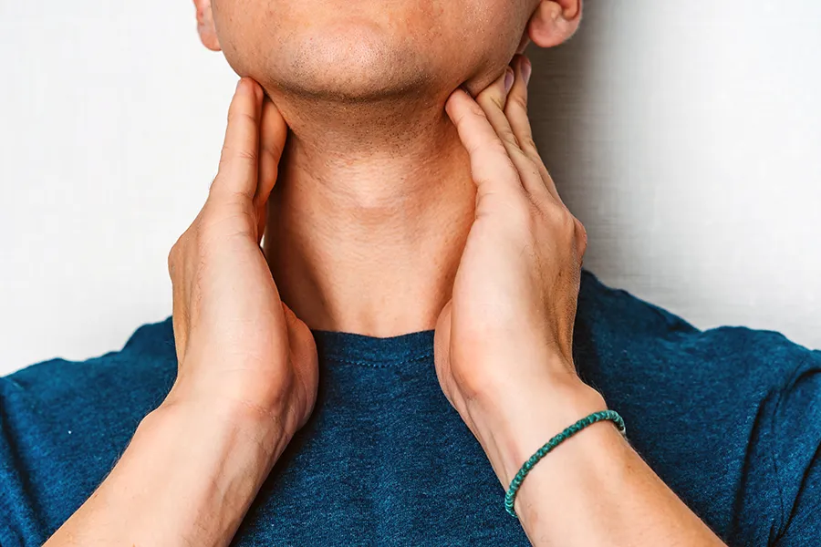 Hypothyroidism-Clinic A man in a dark teal shirt rubs the lymph nodes on his neck. Get hypothyroidism treatment from Anita Petruzzelli, M.D. in Glastonbury.