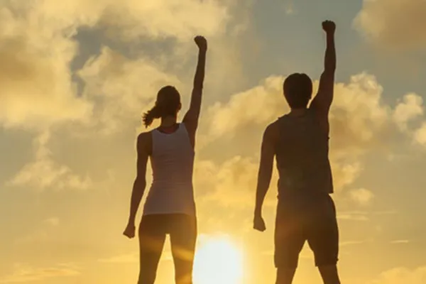 Ipamorelin-Peptide-Clinic A couple raise their right arms in the air in triumph, framed by the sunrise. Get Ipamorelin peptide treatment from Anita Petruzzelli, M.D. in Glastonbury.