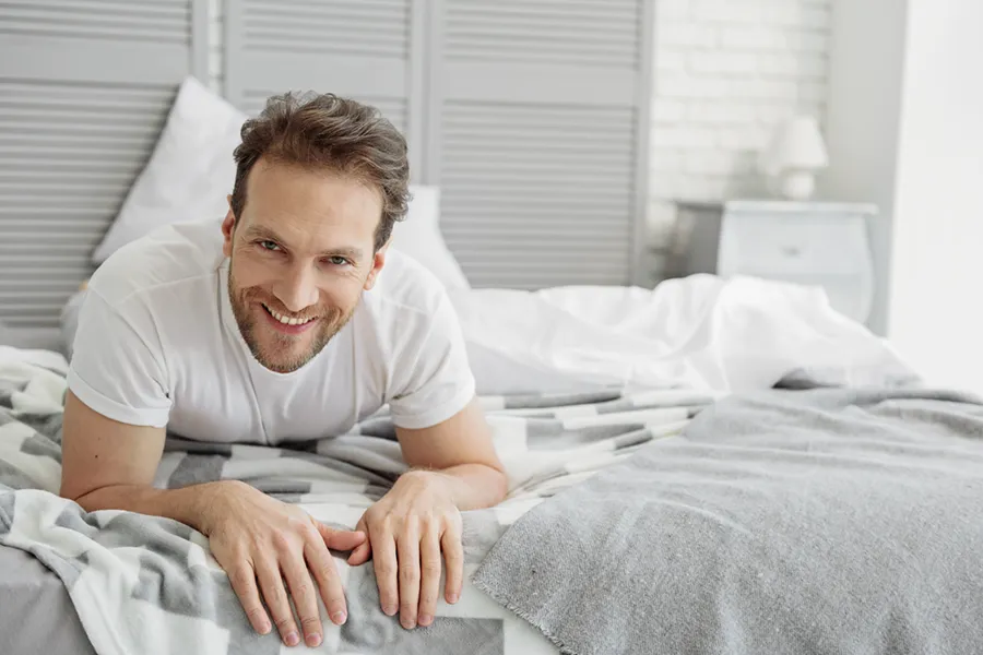 Low-Libido-in-Men-Doctor A dirty-blonde haired man lays on his stomach in bed smiling. Schedule treatment for low libido in men from Anita Petruzzelli, M.D. in Glastonbury.