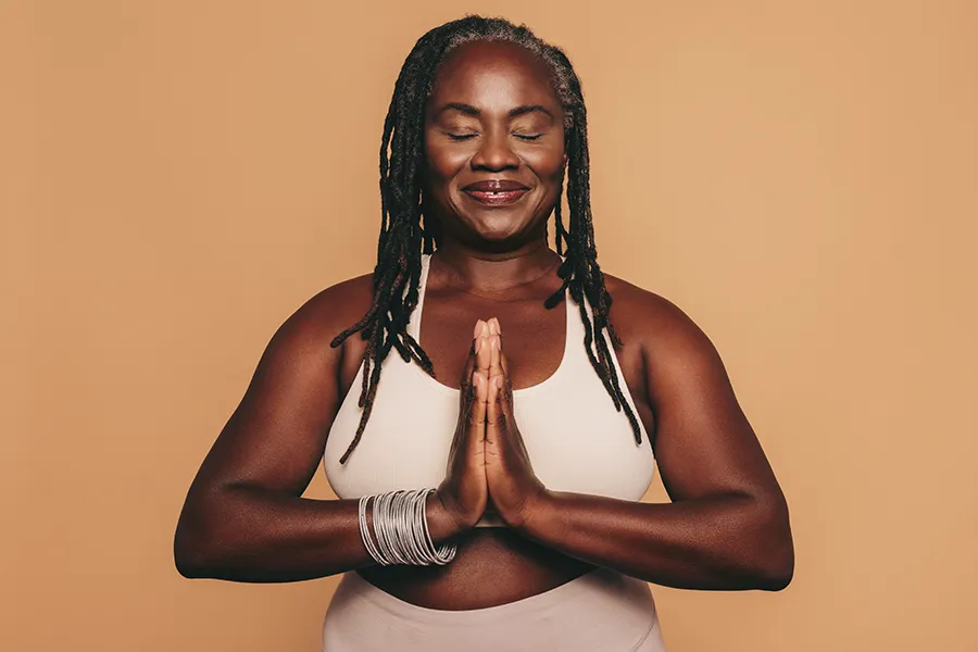 Obesity-Clinic An older African American woman confidently posing against a warm background smiling with hands in a prayer pose. Anita Petruzzelli, M.D. treats obesity using functional medicine in Glastonbury.
