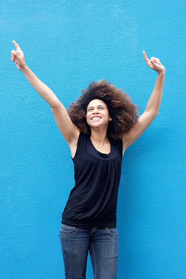 PMS-Treatment A woman in a dark blue tank top standing in front of a bright blue wall, raising her arms in celebration of relief from PMS from Anita Petruzzelli, M.D. in Glastonbury.