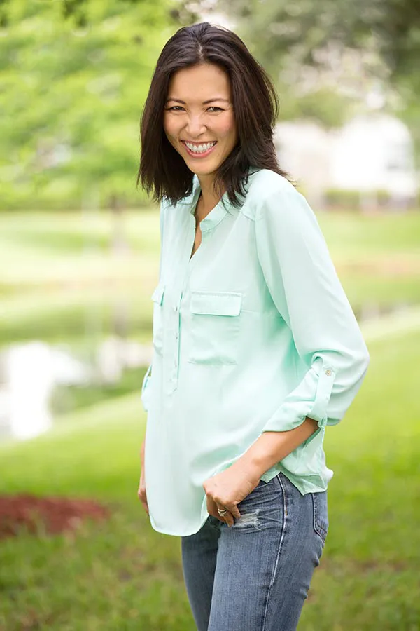 Perimenopause-Treatment A middle-aged brunette woman in a light green button-up shirt stands outside smiling, happy with her perimenopause treatment from Anita Petruzzelli, M.D. in Glastonbury.