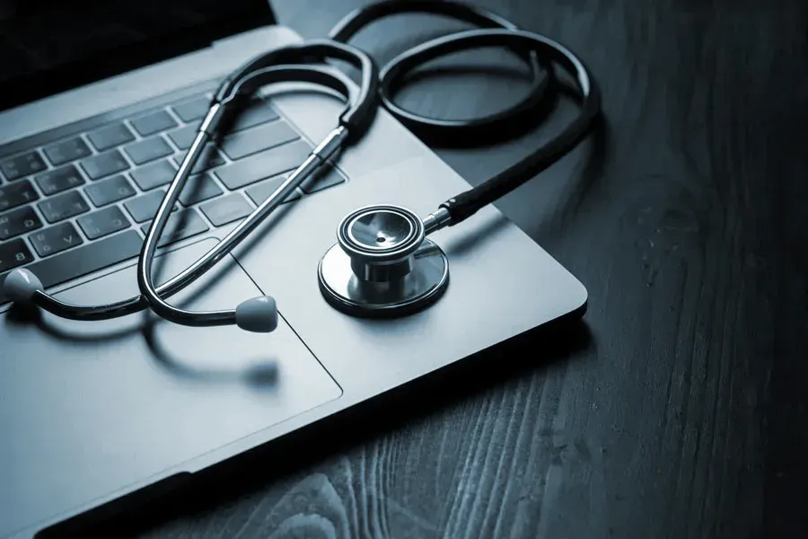 Telemedicine-Doctor An open laptop with a stethoscope lying on it on a wooden table, symbolizing telemedicine care from Anita Petruzzelli, M.D. in Glastonbury.