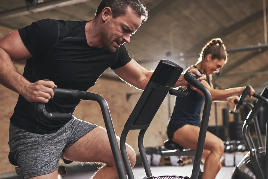 Tirzepatide-Doctor A couple in a brick gym work as hard as they can on exercise bikes, inspired by successful Tirzepatide treatment from Anita Petruzzelli, M.D. in Glastonbury.